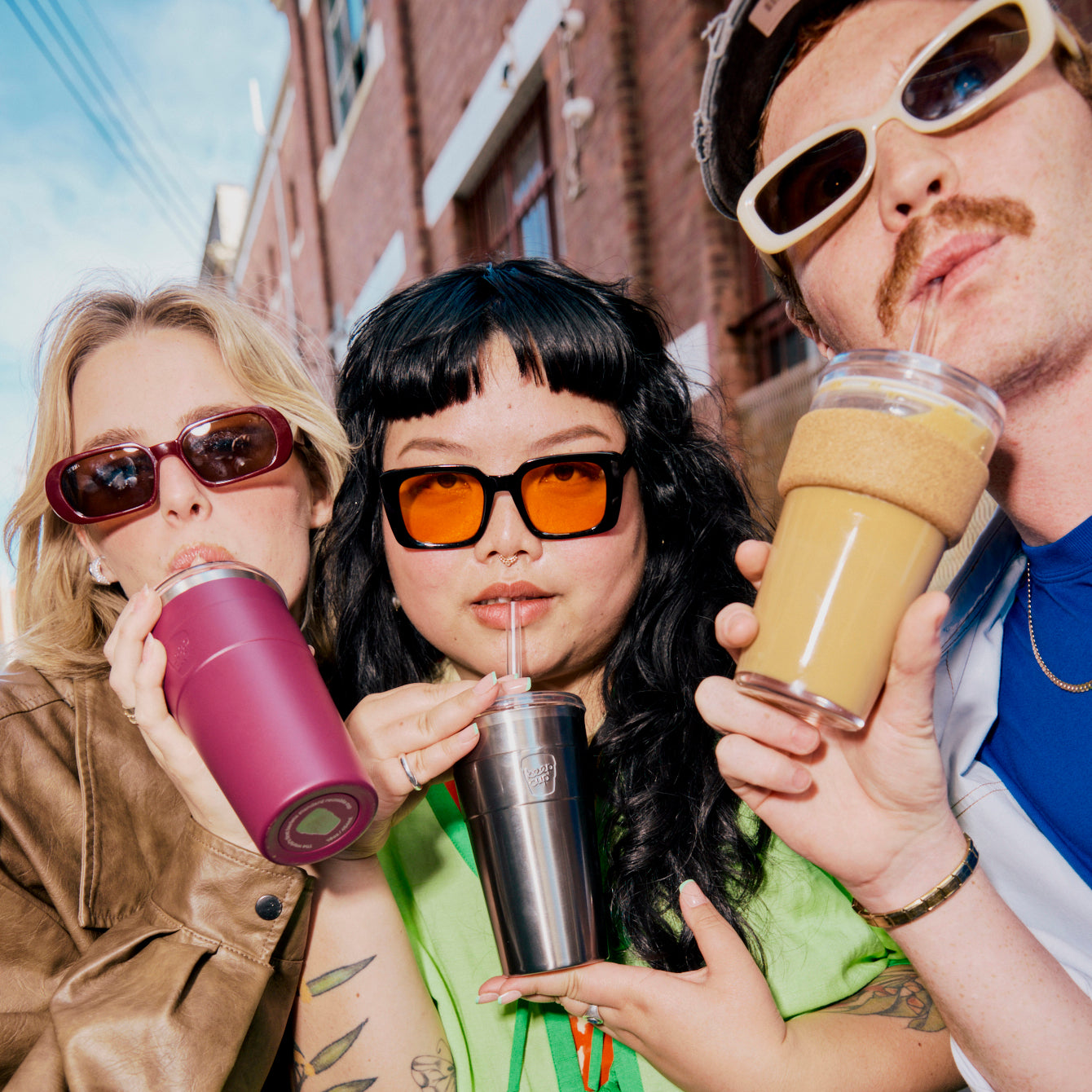 Three people drinking from insulated cups on a sunny street.