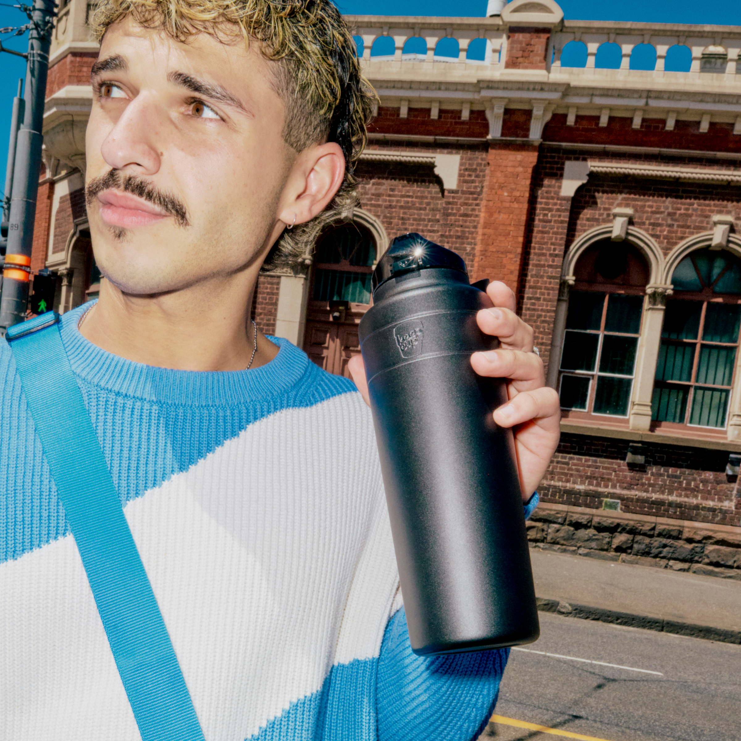 Man holding a black insulated bottle with a building in the background
