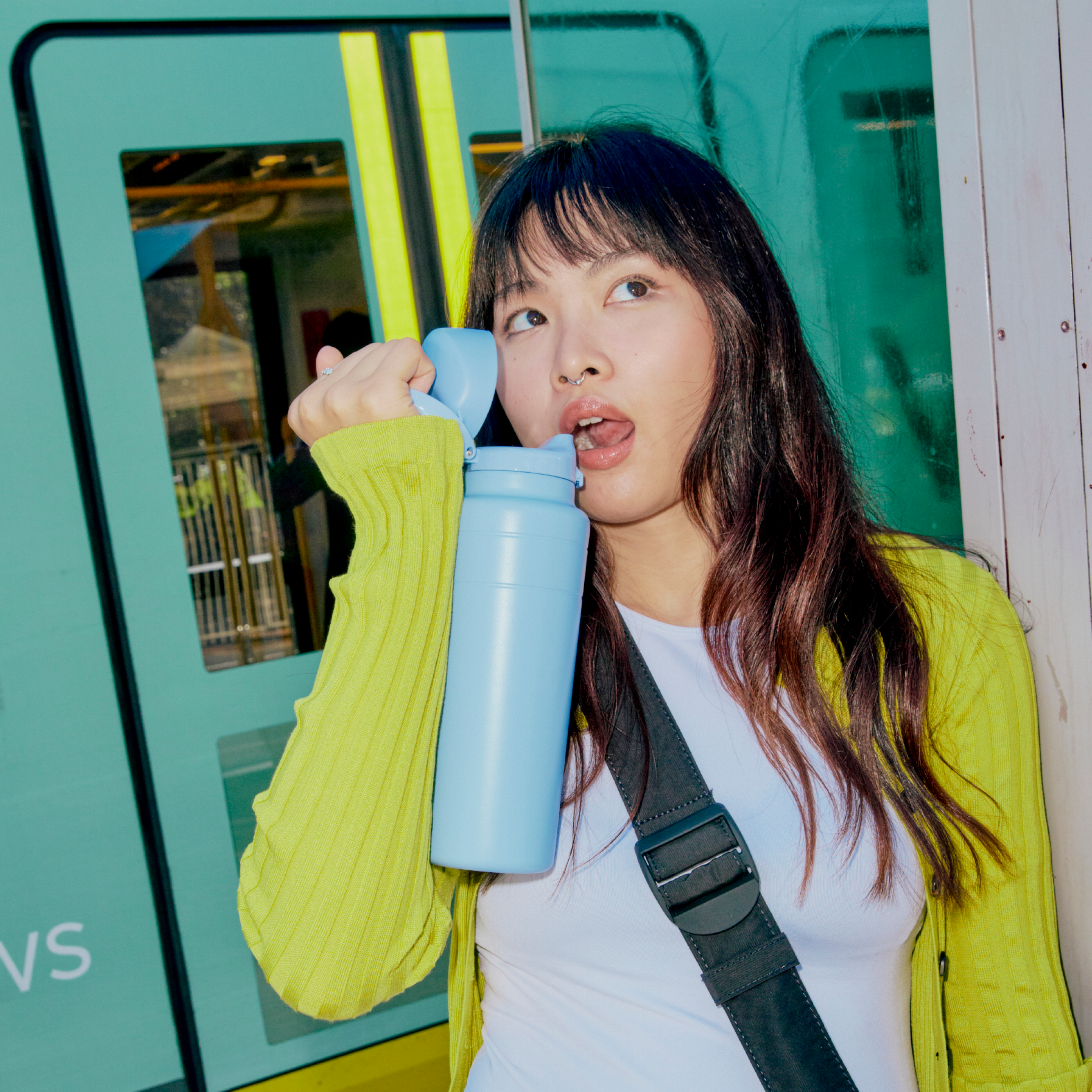 Woman holding an orchid water bottle with a green train in the background