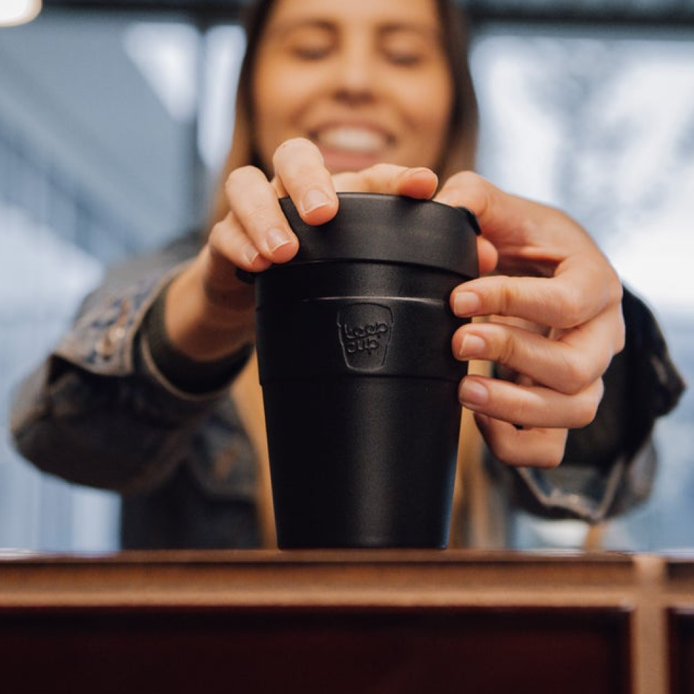 Person holding a black KeepCup stainless steel reusable coffee cup with a blurred background