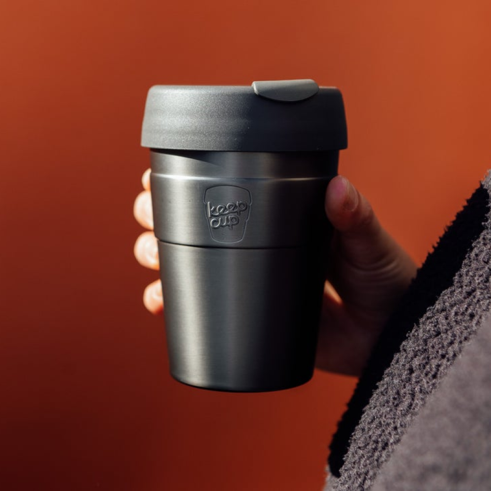 Person holding a KeepCup Thermal stainless steel cup against an orange background