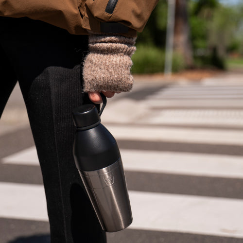 Person holding a black insulated water bottle outdoors on a concrete surface.