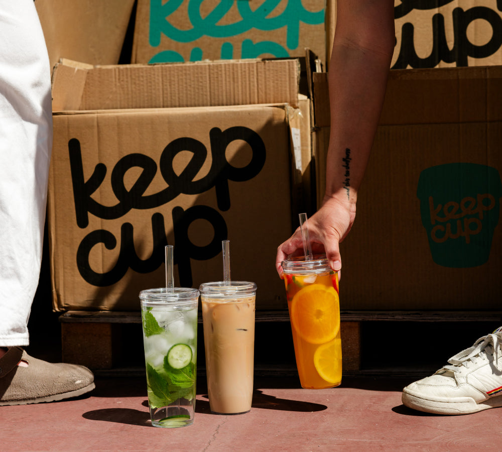 Three filled KeepCup clear reusable iced coffee cups beside KeepCup cartons