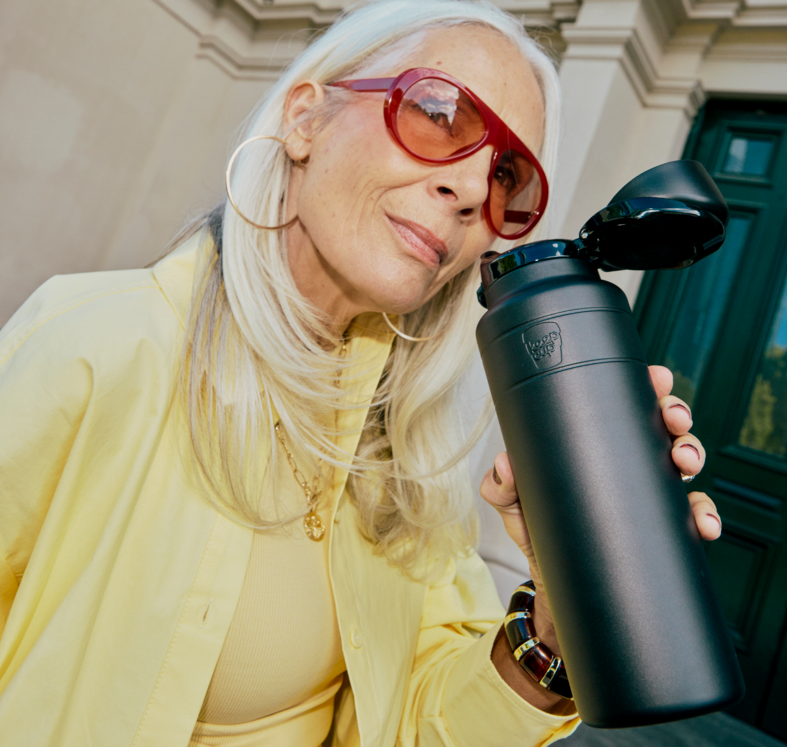 Woman in yellow with long grey hair holding black 950ml Ora Bottle