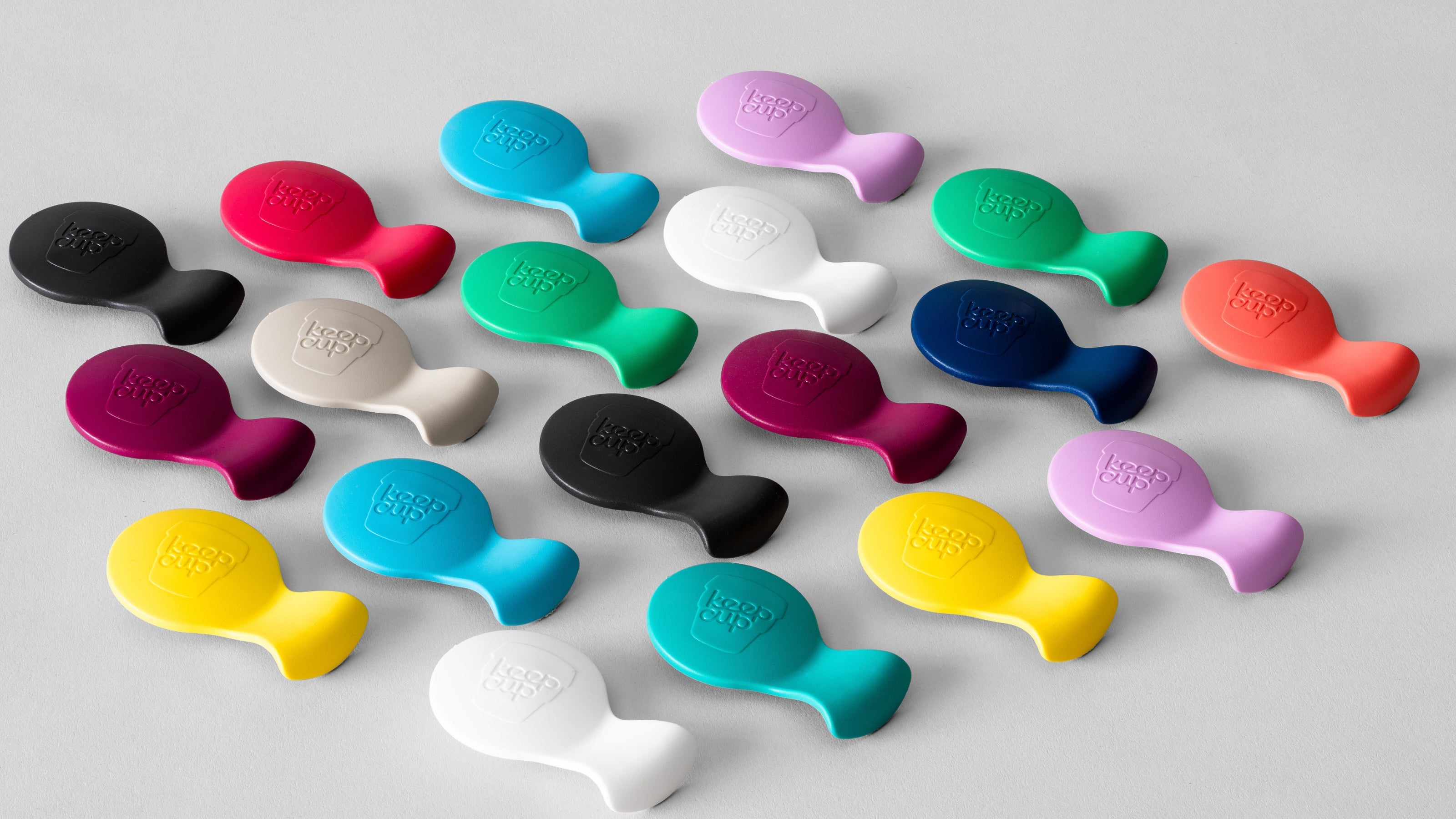 Colourful silicone phone grips in various bright colours including pink, blue, green, yellow, black and white scattered on grey background