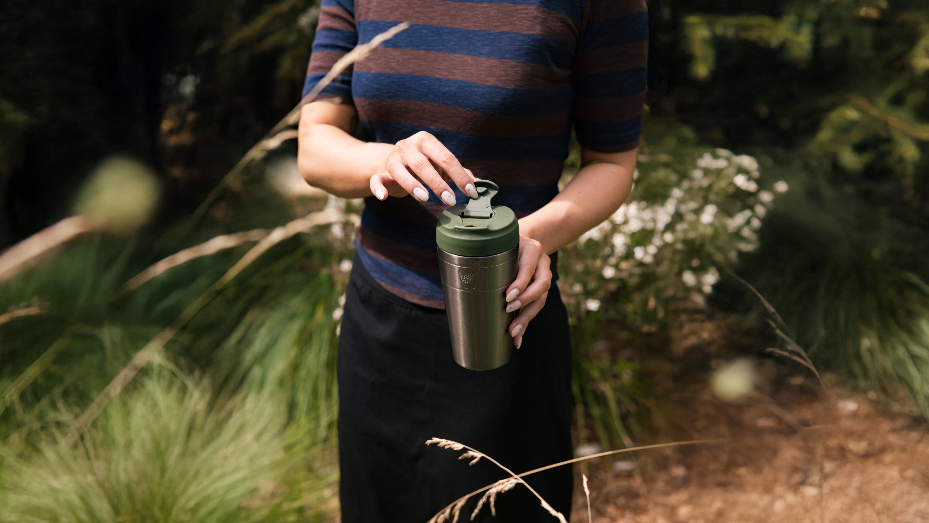 Person holding a silver water bottle with a green cap outdoors