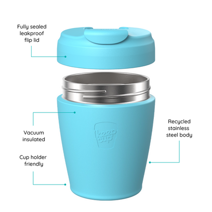 A light blue reusable KeepCup travel cup with a matching lid shown on a white background, with callout lines and text explaining features such as a sealed leakproof flip lid, vacuum insulation, recycled stainless steel body, and cup holder friendliness.