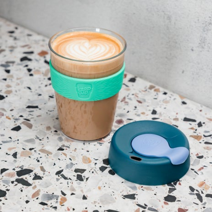 KeepCup reusable coffee cup with a teal silicone band and lid on a terrazzo countertop.
