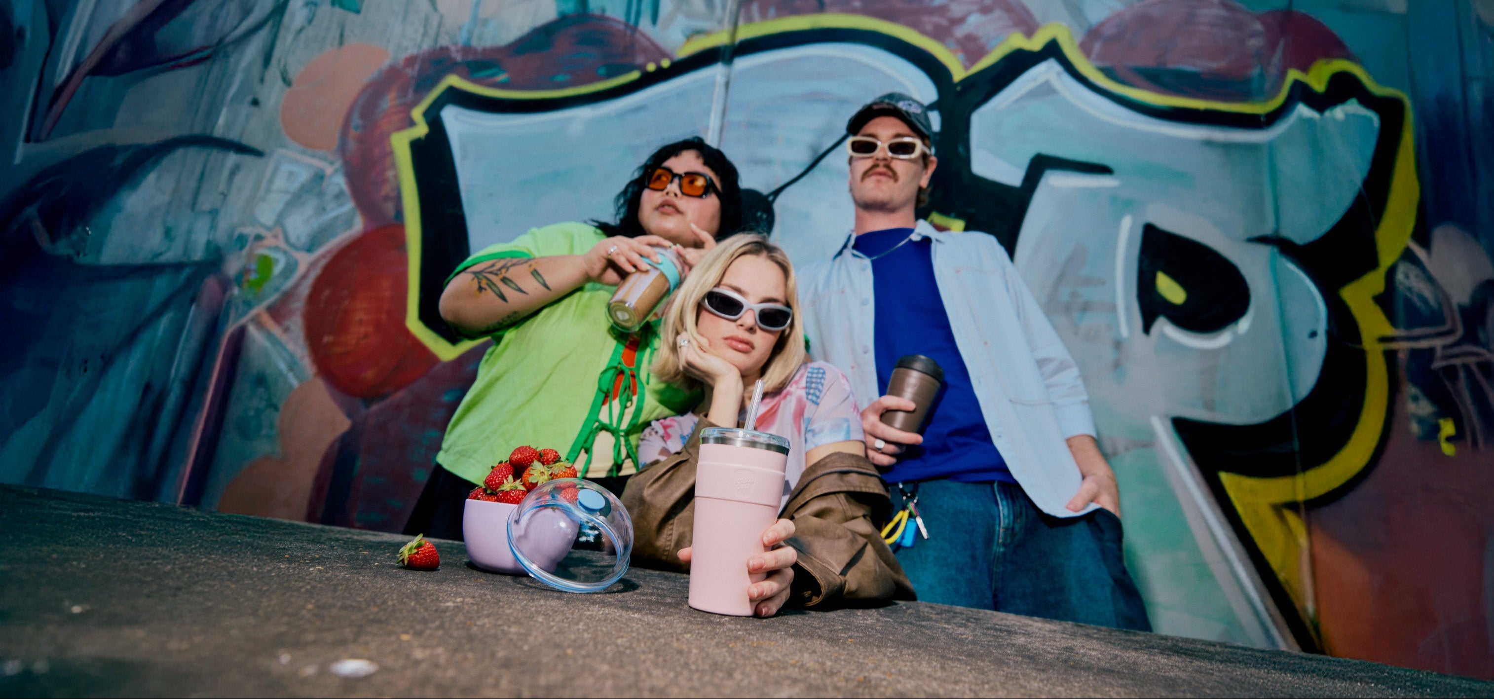 Three people posing in front of a colorful graffiti wall.
