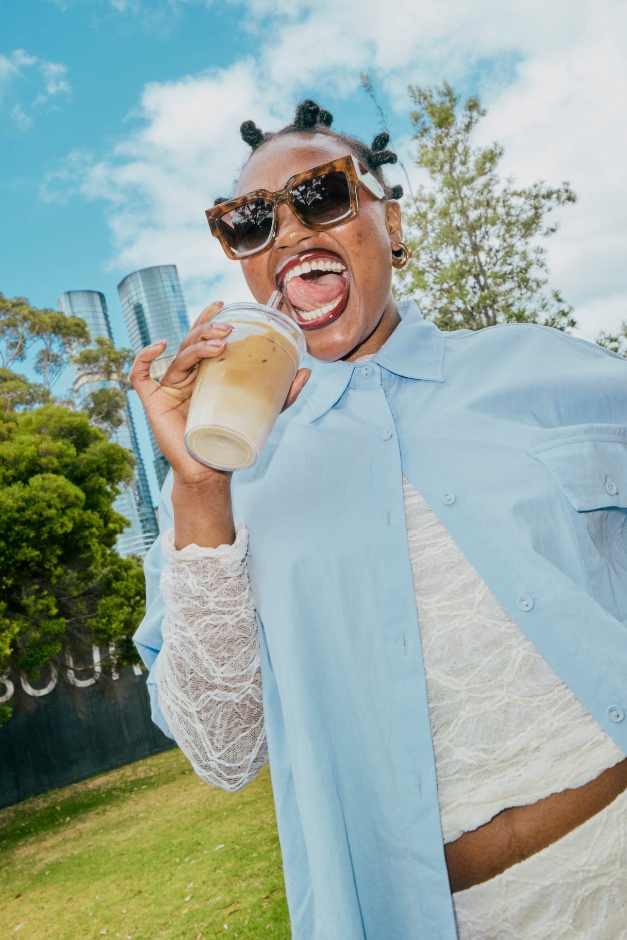 Person holding a drink and a cold cup outdoors with trees and blue sky in the background