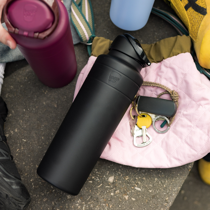 Black water bottle on a concrete surface with a mulberry bottle and keys in the background