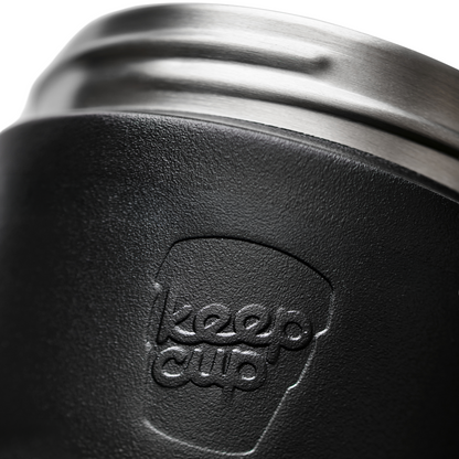Close-up of a black textured insulated KeepCup commuter travel mug with a brushed silver metal rim and an embossed KeepCup logo on the front.