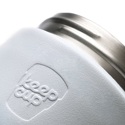 Close-up of a white textured KeepCup insulated cup with a brushed stainless steel rim and embossed KeepCup logo.