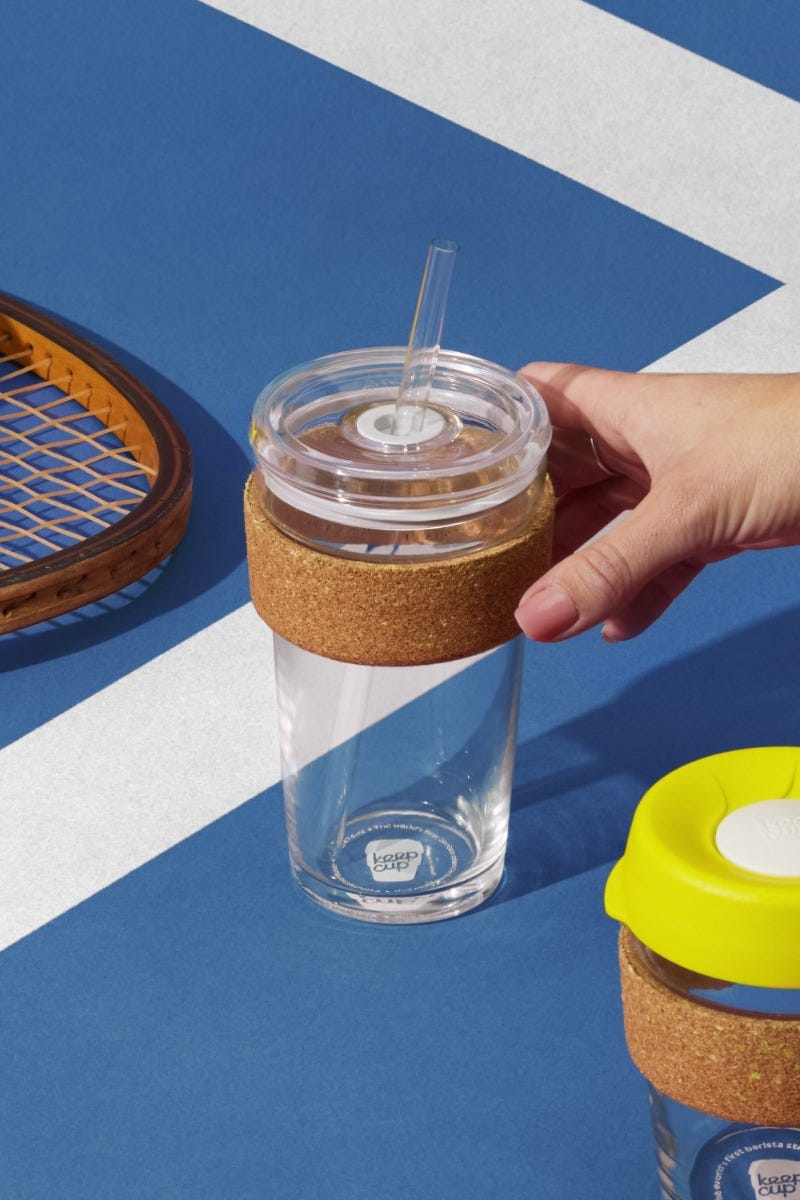 Woman holding KeepCup Sip & Chill Brew Cork Ace reusable glass cup on blue tennis court