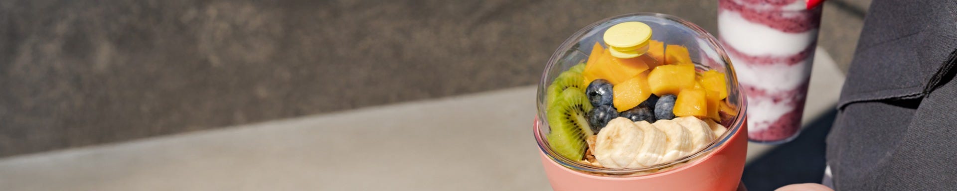 A woman crossing the street holding a KeepCup Cold Cup Original filled with a smoothie and KeepCup Go Bowl in Clay filled with fruit and acai.